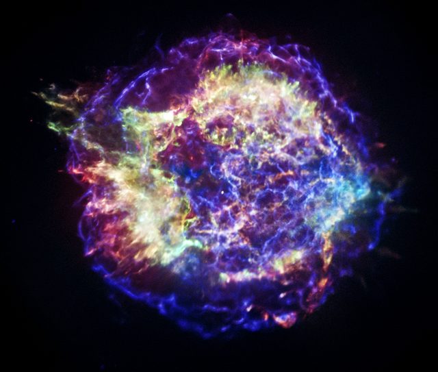 Figure 1. Cassiopeia A is a supernova remnant, that is, what a supernova explosion left behind more than 13,000 years ago. In spite of being far from us (3,400 pc) this is a extremely bright radio source. This picture was constructed by the combined effort of infrared Spitzer Space Telescope (red), Hubble Space Telescope at visible wavelengths (orange), and Chandra X-ray Observatory (blue and green). Credit: NASA/CXC/SAO